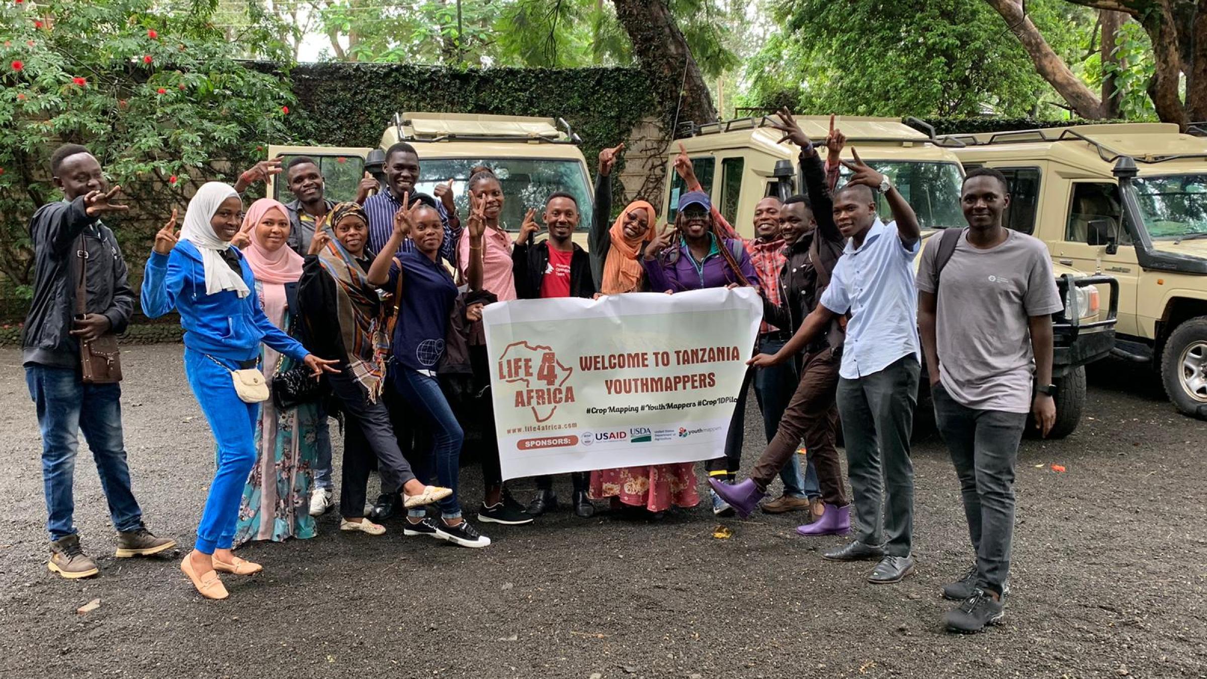 A group of 14 YouthMappers from Tanzania pose in front of jeeps before going out into the field for research.