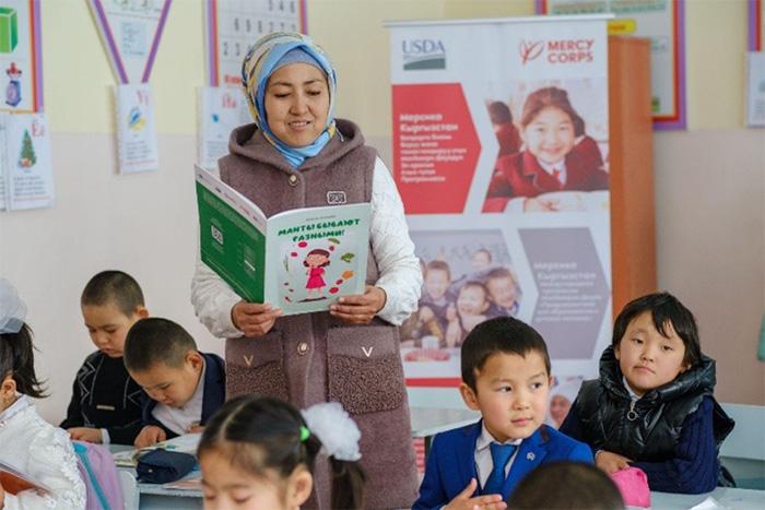 Teacher reading a book about healthy nutrition to school children. Uchkun village, Kyrgyzstan. Photo credit: Mercy Corps staff.